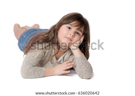 Cool brunette long haired little girl is lying on the light gray background. The girl is supporting her head with one hand.