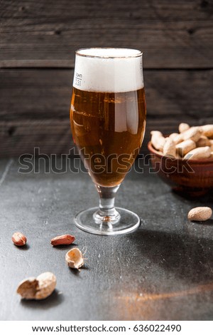 glass of light cold frothy beer, nuts on an old wooden background on stone table with peanuts