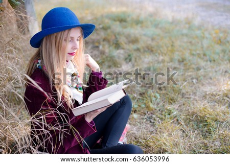 portrait of young beautiful blond hipster woman reading paper book on sunny autumn day outdoors copy space background