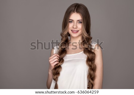 Young attractive blond girl holding myself for long braids. Portrait of beautiful smiling woman with beauty hair. A wide braid. Isolated on gray background Royalty-Free Stock Photo #636064259
