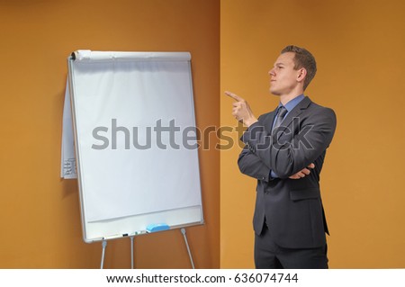 Young businessman points with his finger to a flip chart in the office - isolated with copyspace. Sceptical, critical or analyzing expression for advertisement.