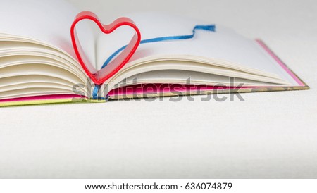 Red heart over diary book with bookmark on white table