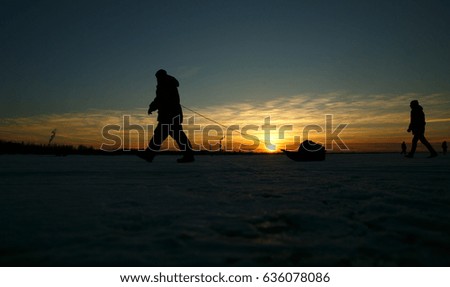 The fisherman's silhouette with the sledge of the gulf going on ice against the background of the orange sunset sky. winter fishing. Ice fishing. Leisure. Winter landscape. Fisherman on ice. lifestyle