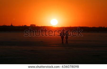 Silhouettes of the man and woman walking on gulf ice against the background of the orange sunset sky. Winter landscape. Winter sunset sky.Winter scene. Fantastic evening winter landscape.Beauty world.