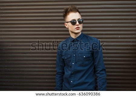 Fashionable handsome young man in sunglasses posing near metal wall