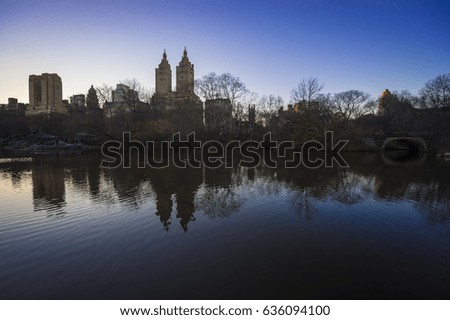 Scenic evening view of the Upper West Side skyline reflected with the silhouettes of bare trees in the lake in Central Park, New York City