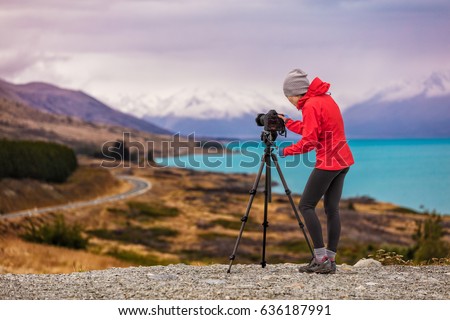 Photographer taking New Zealand travel nature photography. Woman photographer shooting with tripod and slr camera in sunset with beautiful landscape in background.