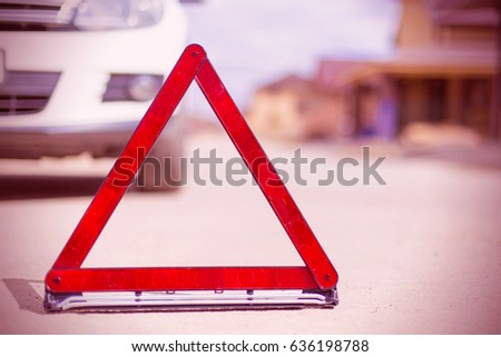 Red broken stop triangle sign on asphalt and blurred car against