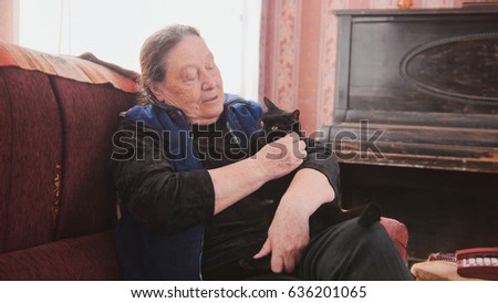Portrait of happy old lady at home - senior woman sits on sofa with black cat - close up