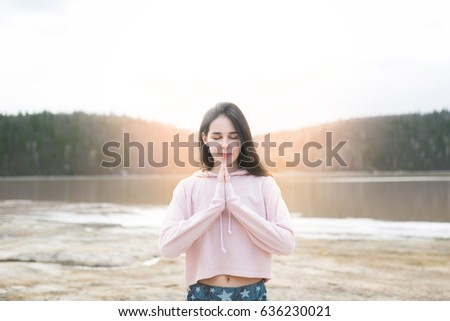 Young woman peaceful meditating by the lake. Fitness girl doing yoga at morning sunrise in nature background