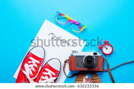 photo of sheet of paper My Vacation, colorful glasses, alarm clock, gumshoes and retro camera on the wonderful blue studio background