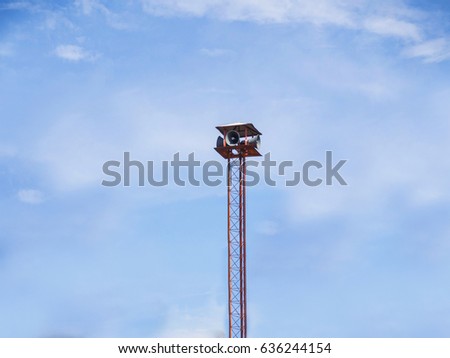 Many speakers on a high red tower against a blue sky background. 
