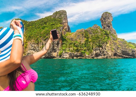 Traveler woman in bikini and big hat standing on wooden boat using smartphone take photo, Koh Kai island, Andaman sea, krabi, Thailand
