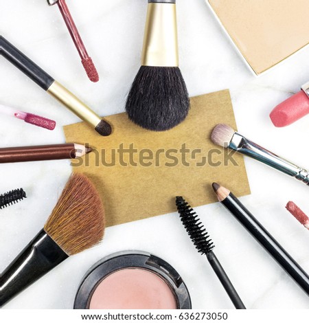 Makeup brushes, pencils, lipstick et al on a light background, with a blank kraft business card for copy space. A square template for a makeup artist's business card or flyer design