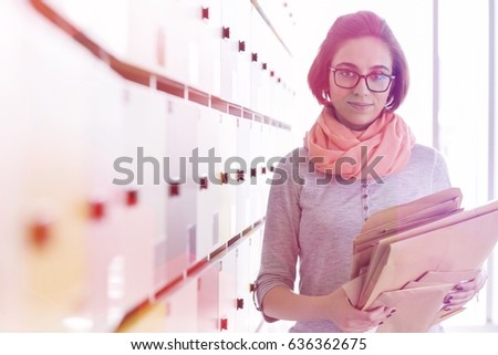 Portrait of creative businesswoman holding envelopes in locker room at office