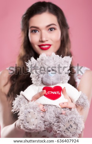 Beautiful girl with long hair holds a toy bear on a pink background