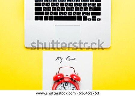 photo of sheet of paper My Book, cool laptop and red alarm clock on the wonderful yellow studio background