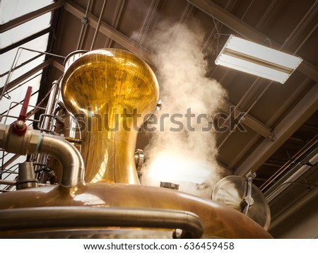A photograph of a pot still in a whiskey distillery. Steam is rising from the still to the top of warehouse as the still is going through a distillation process. Royalty-Free Stock Photo #636459458