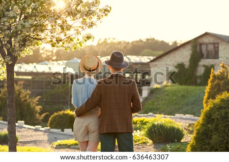 A couple in love at sunset in hats stand with their backs in the frame. American dream. A retro couple in his country house, his estate. Lavstory, family day, St. Valentine's Day. Royalty-Free Stock Photo #636463307