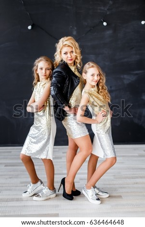 Stylish mother and twins in golden dresses in studio hugging and having fun