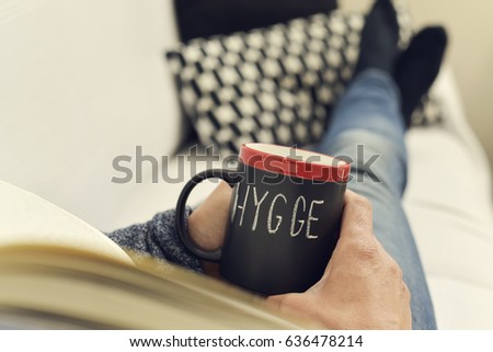closeup of a young man reading a book with a cup of coffee in his hand with the text hygge, a danish and norwegian word for comfort or enjoy, which can be a whole philosophy of life Royalty-Free Stock Photo #636478214