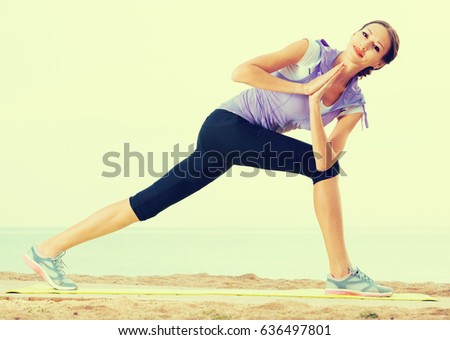 Ordinary woman exercising yoga poses standing on sunny beach by ocean in morning
