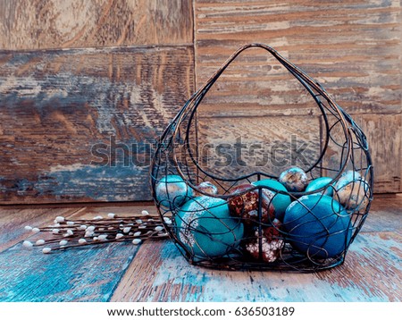 On the old wooden shabby table a dish of metal with painted in a different color Easter eggs chicken and quail and Golden blue green purple feathers, willow