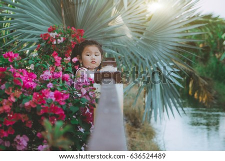 vintage tone picture of outdoor sad little girl standing in a field with flowers and river side.
