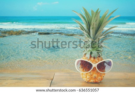 Pineapple with sunglasses on wooden table. Beach and tropical theme.