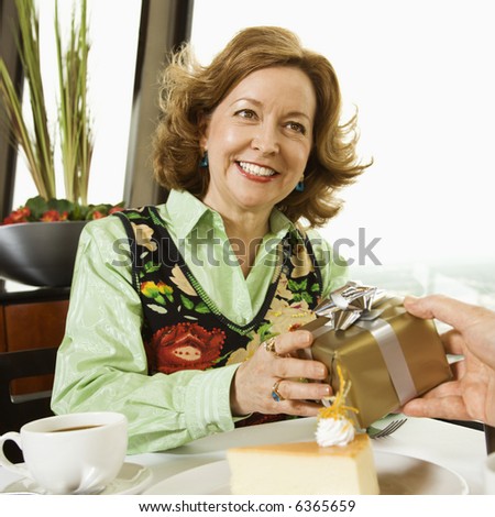 Mature Caucasian couple having dinner in nice restaurant as man gives gift to woman.