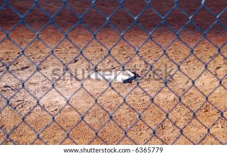 The home plate of a baseball diamond, with the chain link fence of the batter's box slightly out of focus.