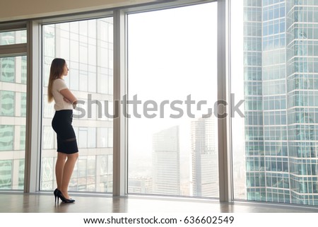 Young woman standing near skyscraper window and looking on urban landscape. Businesswoman thinking about plans on future while contemplating the cityscape. Inspiration in business concept. Copy space 
