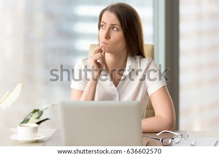 Woman with pensive facial expression looking aside while sitting at workplace. Unsure businesswoman thinking about difficult question. Female office worker doubted because of uncertain situation  Royalty-Free Stock Photo #636602570