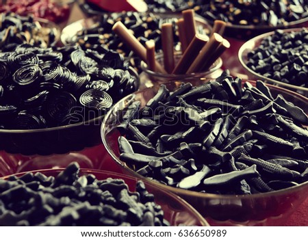 Black candy licorice of different shapes in a bowl on the table. Photo in blue shade key in the style of instagram Royalty-Free Stock Photo #636650989