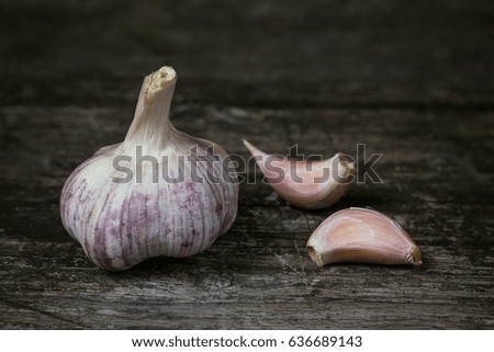 Bulb of garlic and two garlic cloves on an old wooden table. Edited as a vintage photo.