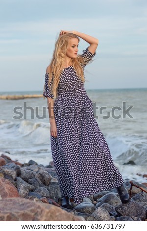 beautiful slender blonde with blue eyes in a long polka-dot dress on a background of azure sea
