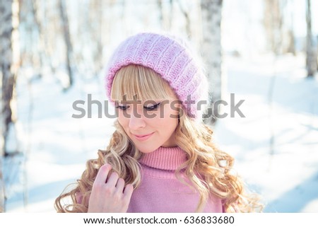 Attractive young woman wearing purple warm coat, white wool knitted cap and scarf in cold winter weather in park.