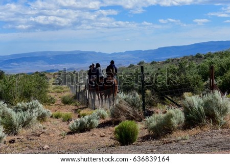 Back view of people on horseback traveling through the southwest landscape of sage and mountains in distance.