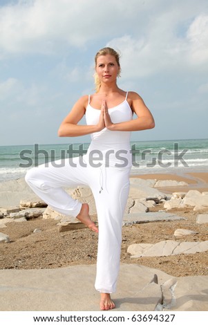 Beautiful blond woman practicing yoga at the beach