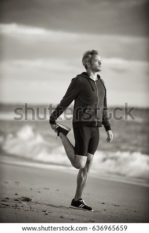 Beautiful gray-haired man in sportswear doing stretches on the beach in the early morning. Black and white picture
