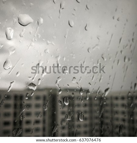 Drops of rain on a window pane, buildings in background, black and white color tone