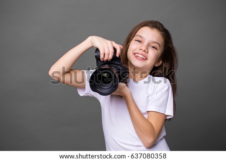 Cute brunette little girl holding an photo camera, isolated on gray background