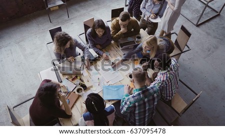 Top view of mixed race business team sitting at the table at loft office and working. Woman manager brings the document. Royalty-Free Stock Photo #637095478