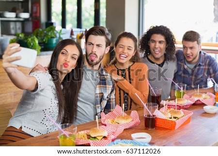 Young woman taking selfie with friends in restaurant