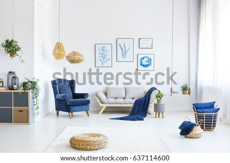 White living room with wood sofa, blue armchair, lamps, posters Royalty-Free Stock Photo #637114600