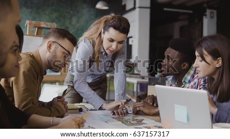 Brunette female team leader talking with mixed race group of people, writes with a marker on the model of house. Royalty-Free Stock Photo #637157317