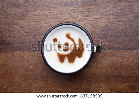 A rustic white mug with coffee cream. Food art creative concept image, cute panda bear drawing with cinnamon powder over wooden background.