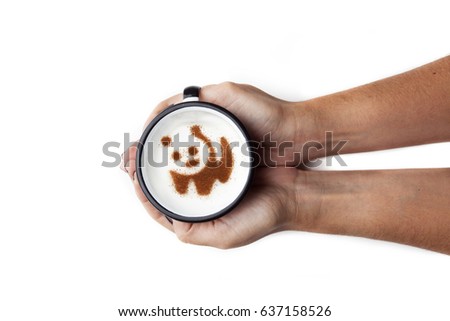 Hand holding a rustic white mug with coffee cream. Food art creative concept image, cute panda bear drawing with cinnamon powder over white background.