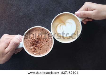 Top view image of man and woman's hands holding coffee and hot chocolate cups with wooden table background
