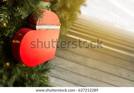 Red? gifts box in the shape of heart in the Christmas tree decorated by light bulbs in the morning light